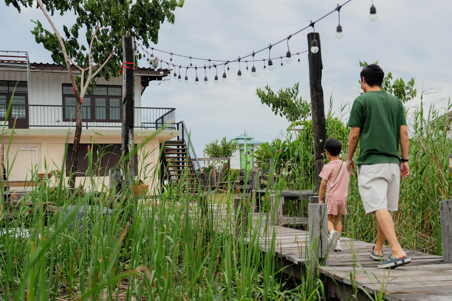 A father and child walking a boardwalk toward a string-lit house