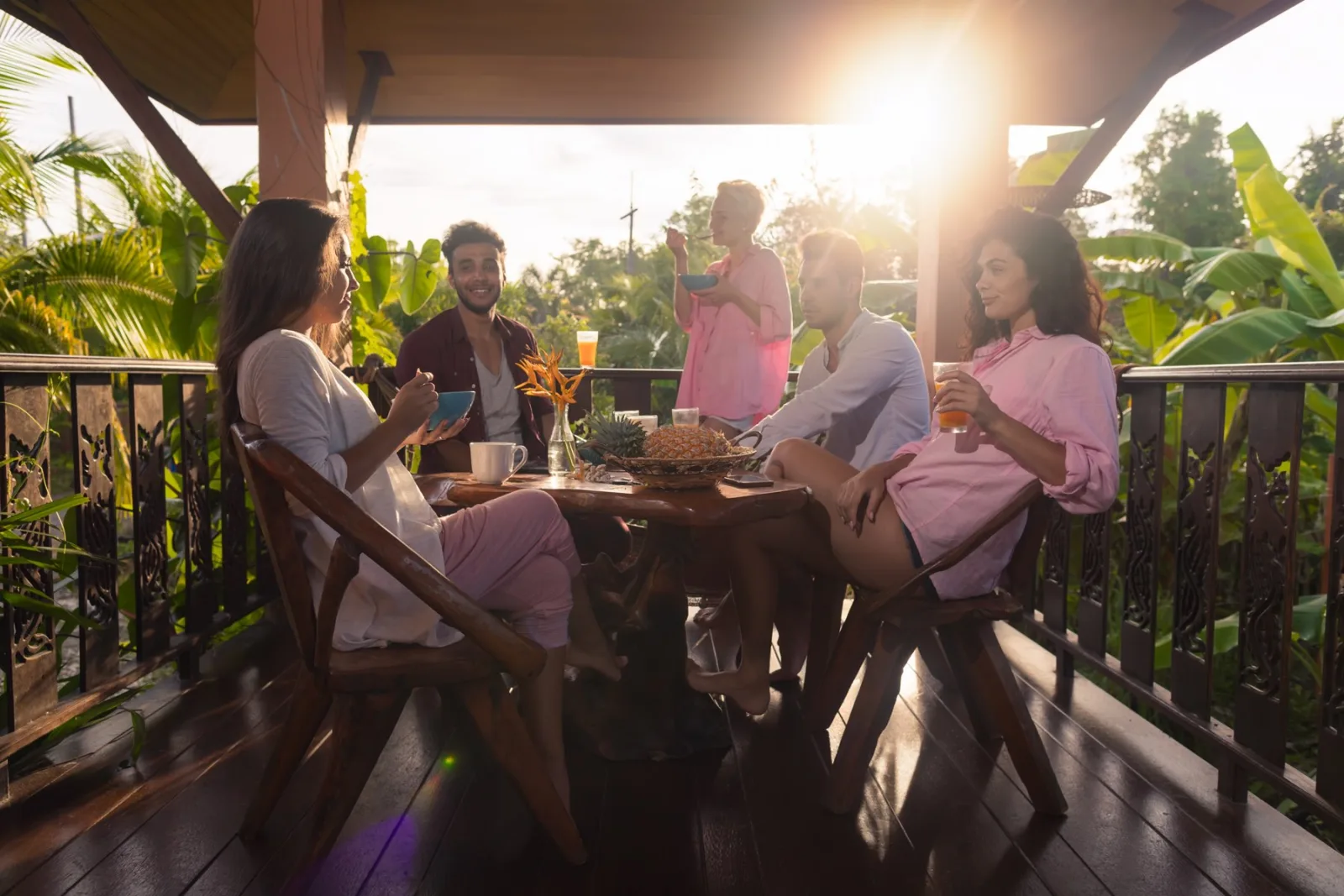 Friends around a long table on a wooden veranda at golden hour